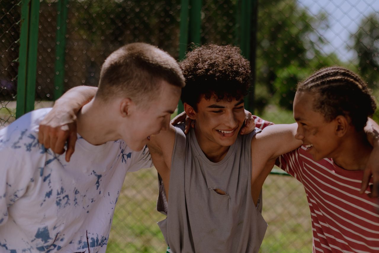 Happy teenagers laughing and embracing outside, showcasing friendship and diversity.