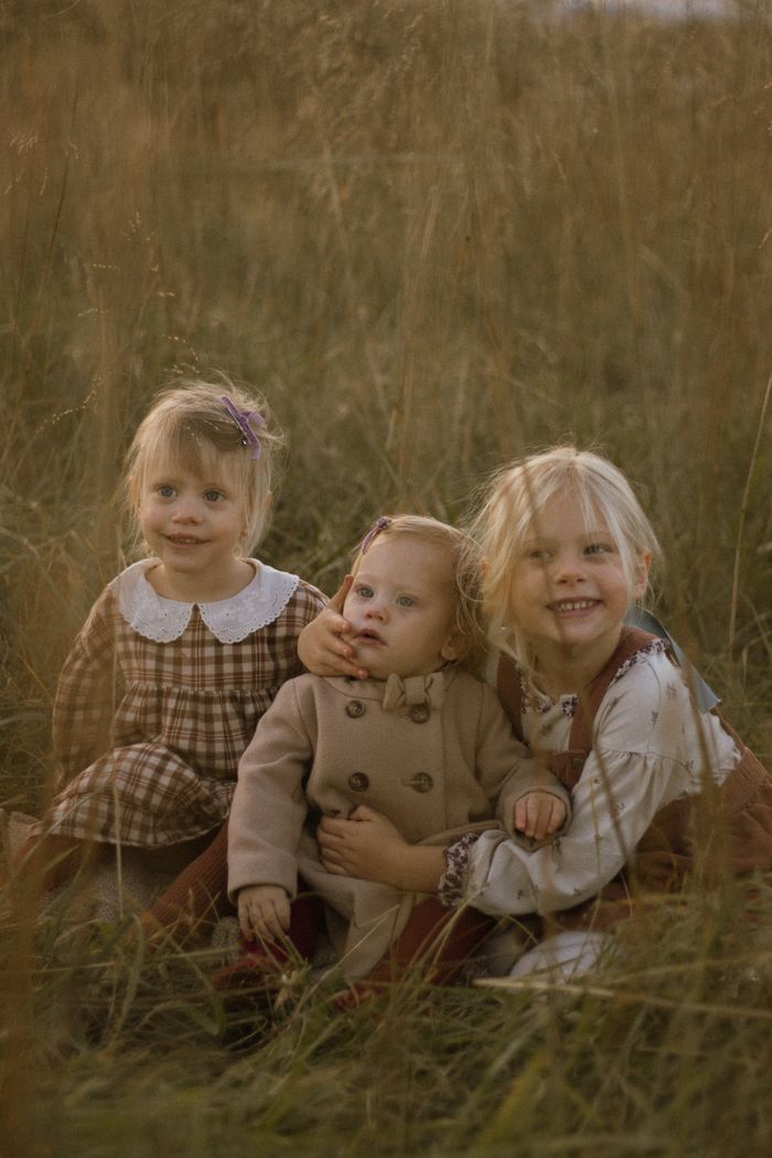 A lovely outdoor portrait capturing three young sisters enjoying a warm, rustic setting.