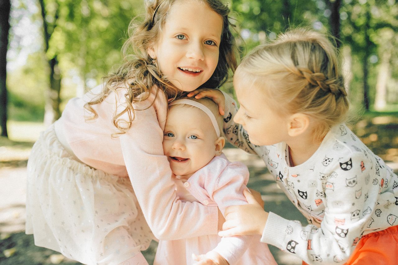 our-experience Three joyful siblings hugging in a sunlit park, capturing the essence of childhood and family closeness.