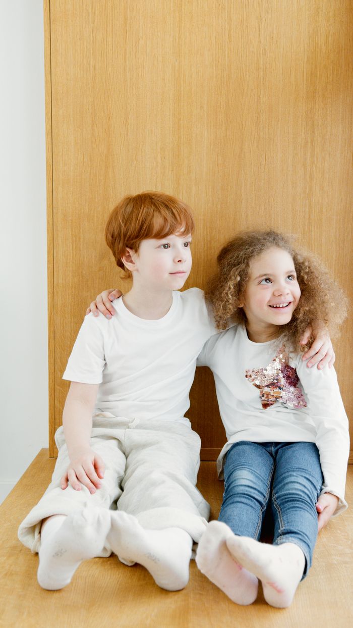 about-img Two children sitting together on a wooden surface, sharing a moment of affection with arms around each other.