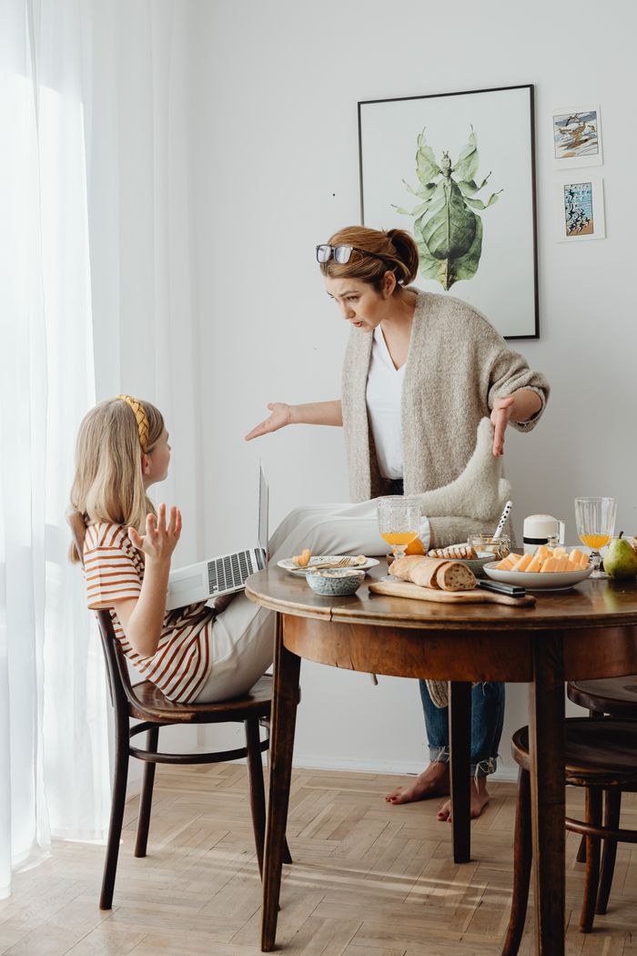 Mother and daughter having a conversation at a breakfast table with food and laptop.
