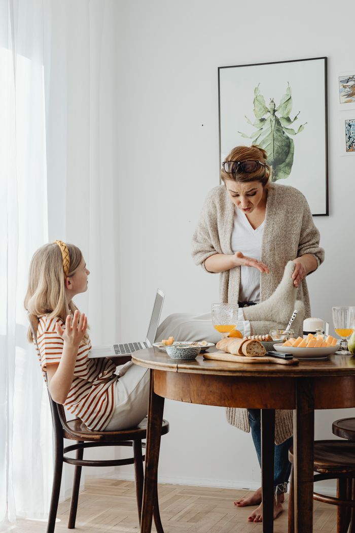 A mother scolds her daughter for having feet on the table during breakfast, highlighting family dynamic.