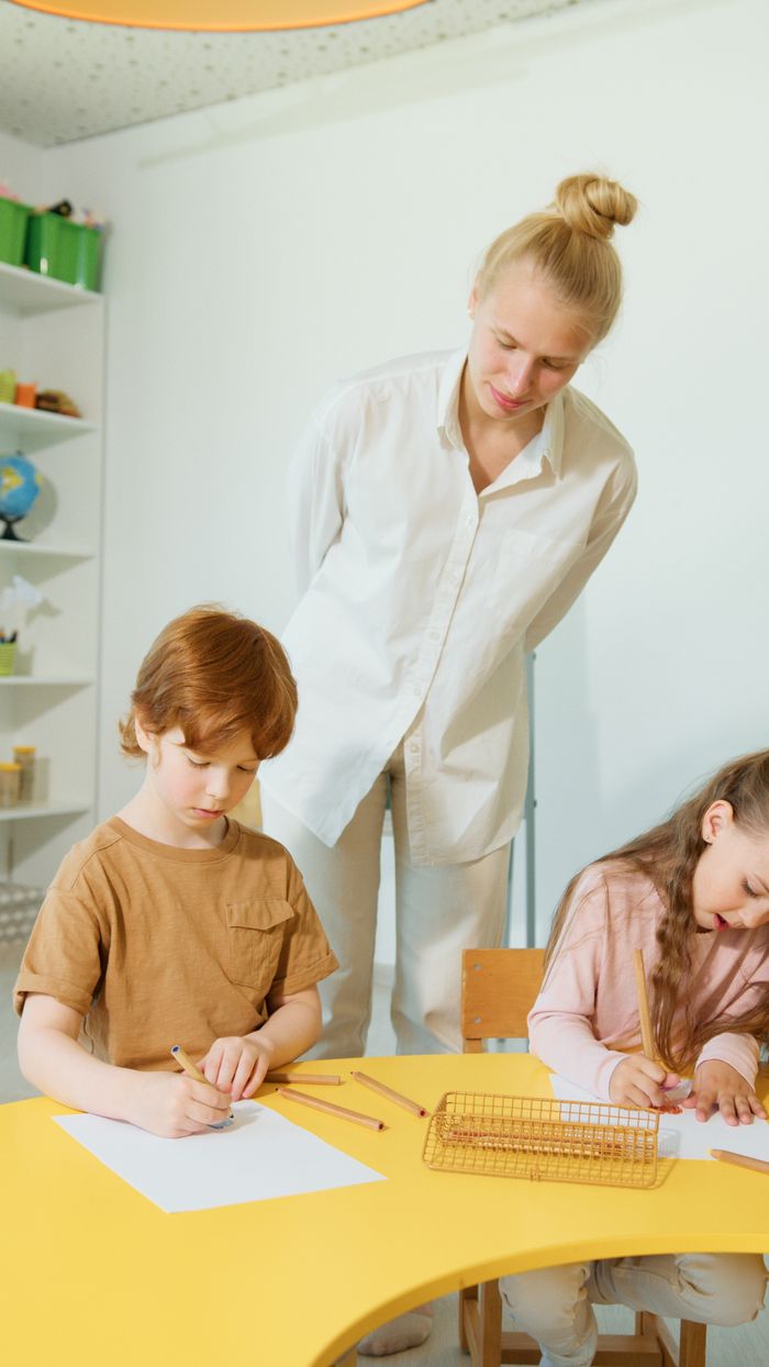 Mastering the First Impression: Your intriguing post title goes here Children focus on schoolwork as a teacher oversees in a bright, modern classroom.